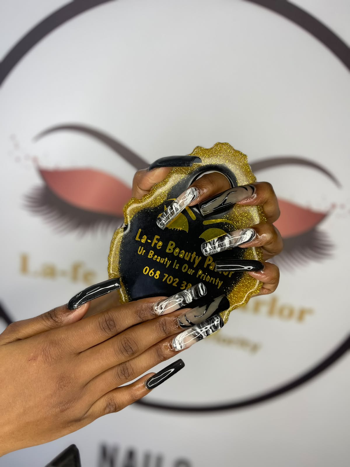 Long square nails in glossy black and black-and-white marble, held over the La-fe sign