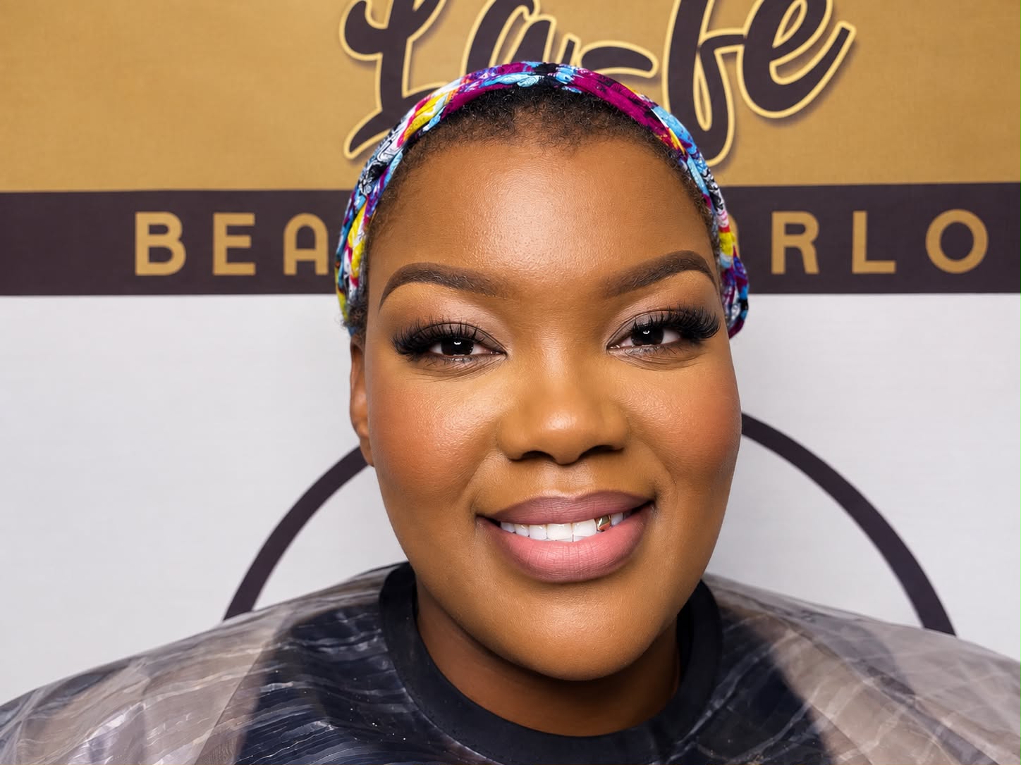 Client with a soft natural beat, full lashes and a pink nude lip, in front of the La-fe Beauty Parlor sign